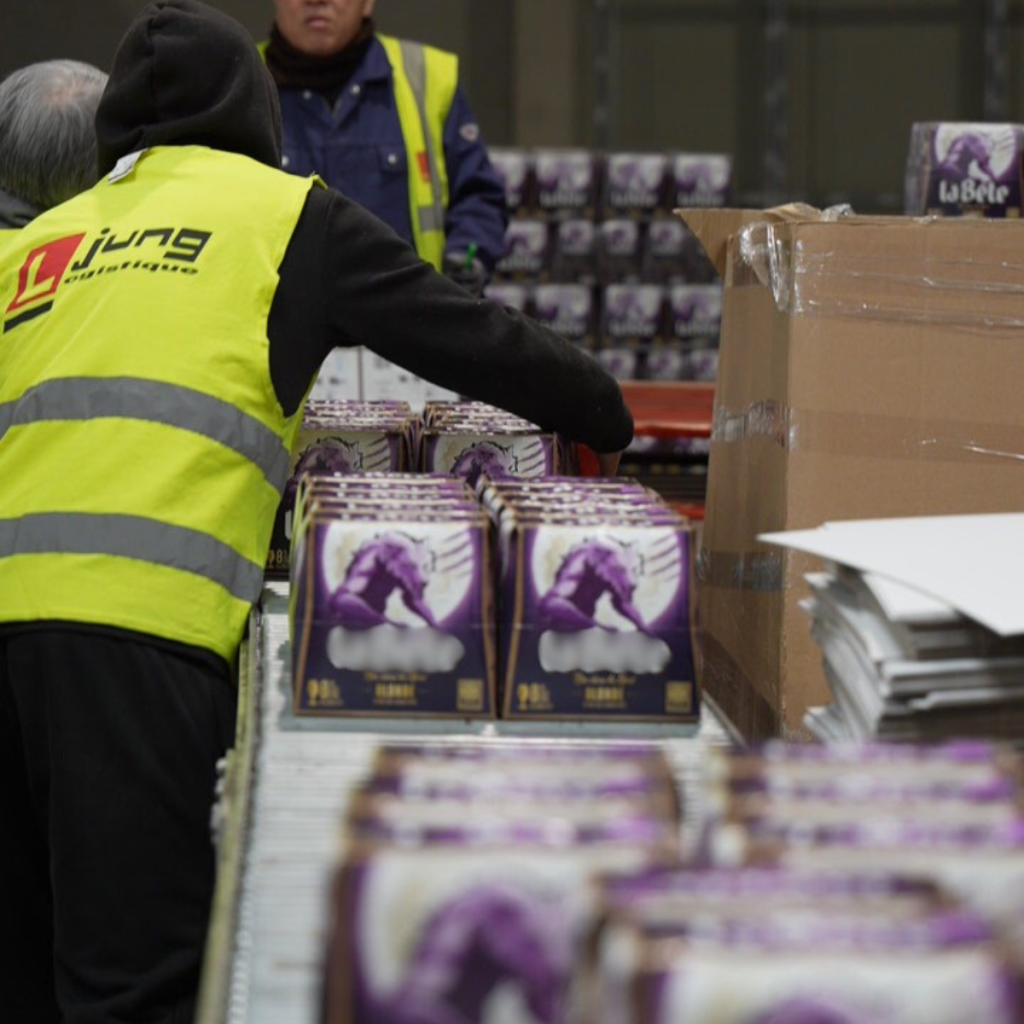 Un préparateur Jung Logistique effectue une opération de co-packing manuel sur des packs de bières dans un entrepôt.