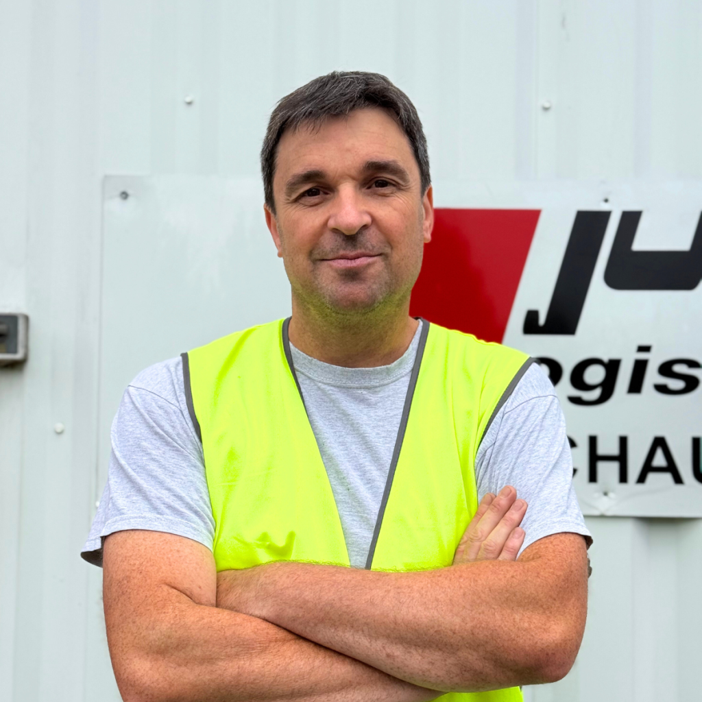 Portrait de Frédérique, chef d’équipe chez Jung Logistique, portant un gilet jaune de sécurité devant le site logistique.