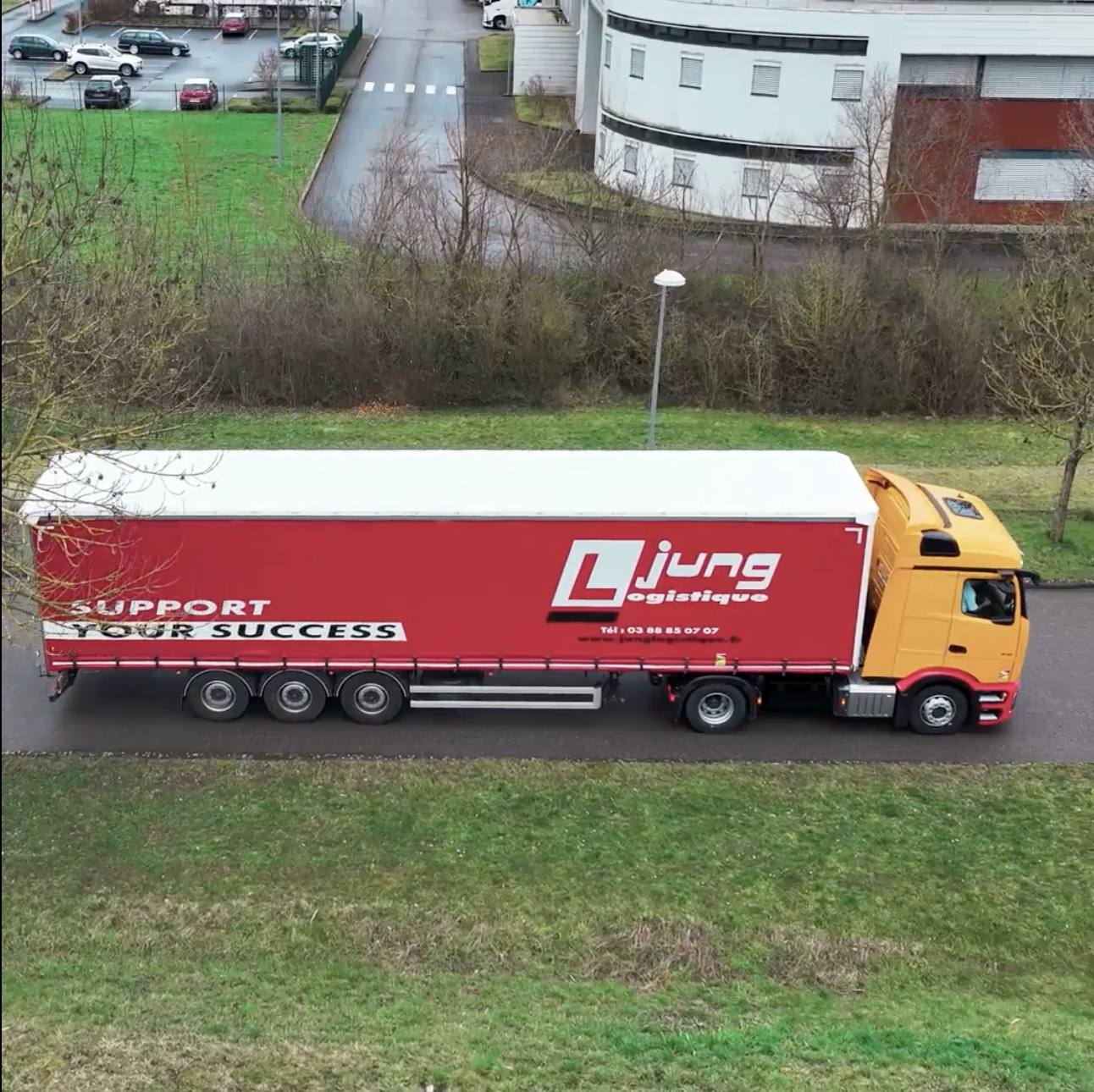 Camion semi-remorque Jung Logistique, cabine jaune et remorque rouge, vu du ciel sur une route de zone logistique, illustrant l’optimisation du transport routier
